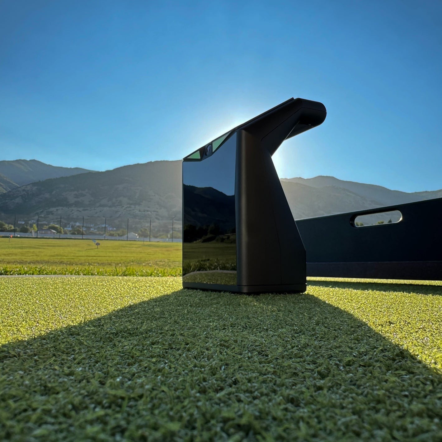 TruGolf LaunchBox launch monitor positioned on a hitting mat at an outdoor driving range with mountains in the background.
